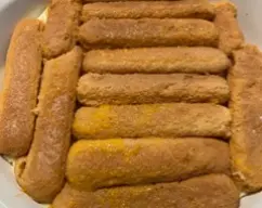 Step <p>Colocamos una capa de bizcochos remojados en la fuente donde vamos a montar el tiramisu.</p><p>Cubrimos con la mitad de la crema de mascarpone que teníamos reservada. </p><p>Repetimos otra capa de bizcochos y terminamos con el resto de la crema.</p><p><br></p> illustration